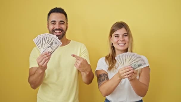 Férfi és nő pár mosolygós magabiztos mutató dollár felett elszigetelt sárga háttér - Felvétel, videó