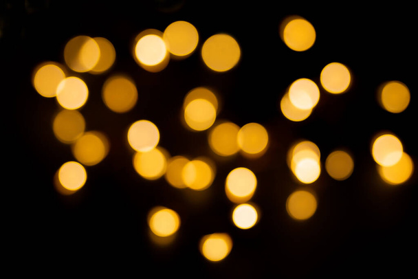 Gelbe und braune defokussierte Lichter auf schwarzem Hintergrund. Verschwommenes Bokeh, Überlagerung. Weihnachten, Neujahr, Feiertag - Foto, Bild
