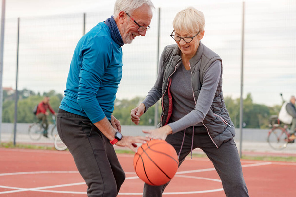 senior woman and mature man playing basketball in the park - Photo, Image