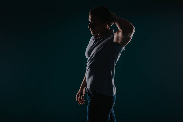 Gespierde en aantrekkelijke man die in een donkere kamer staat en zijn biceps buigt - Foto, afbeelding