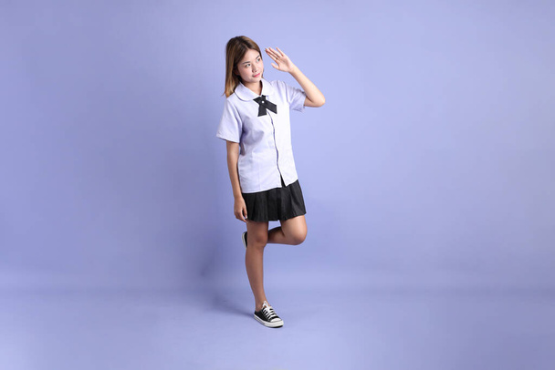 Азіатська дівчина в тайській студентській формі стоїть на фіолетовому фоні. - Фото, зображення