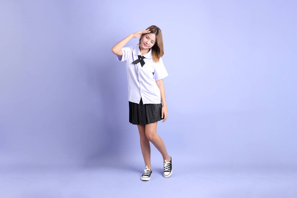 Азиатка в тайской студенческой форме, стоящая на фиолетовом фоне. - Фото, изображение