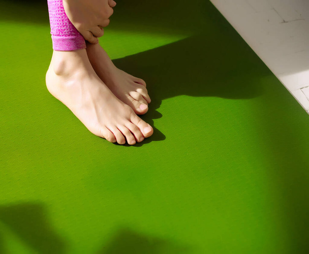 Ženské nohy na zelené podložce jógy uvolňující se po masáži pro uvolnění svalového napětí. Zmírnění bolesti svalů, zvýšení průtoku krve. Fyzioterapie, reflexologie a koncepce podpory flexibility. - Fotografie, Obrázek
