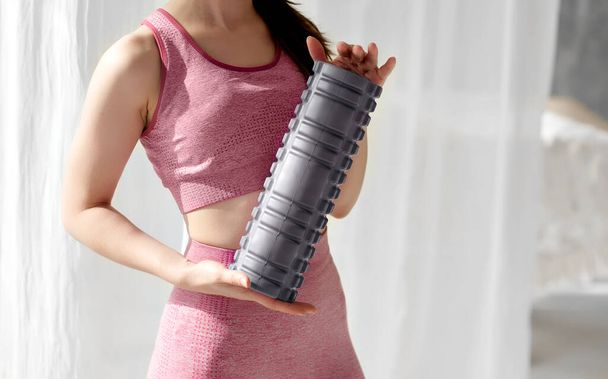 Grey foam roller massager held by a sportswoman. Sports inventory, tools. Lymphatic drainage massage, self-myofascial release, improving flexibility, reducing muscle soreness, increasing blood flow. - Photo, Image