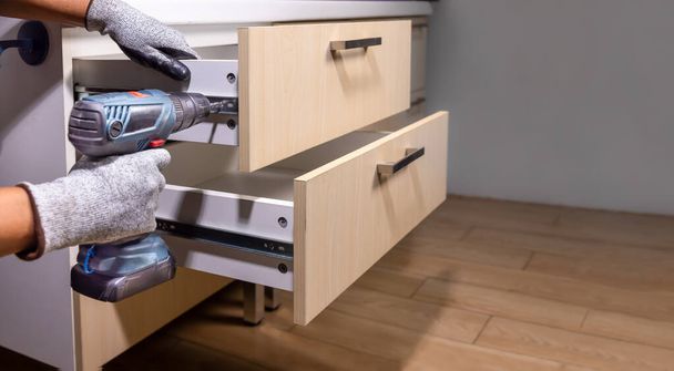 Travailleur fixer sur des glissières de tiroir serré dans la cuisine. Concept Fix glissières de tiroir en bois collé. - Photo, image