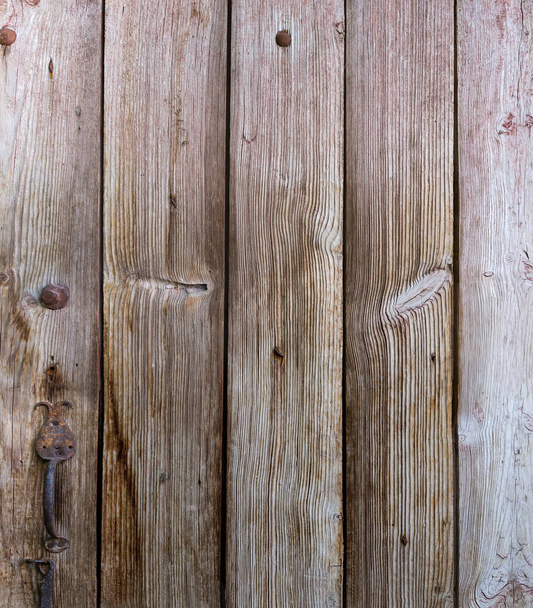 Фрагмент старой деревянной двери, сделанной из грубо обработанных досок с узлами и железной кованой дверной ручкой - Фото, изображение