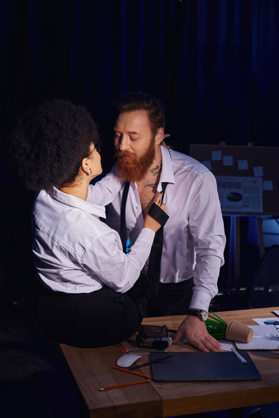 hot african american woman seducing bearded tattooed colleague near mess on work desk in office - Photo, image