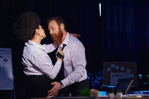 african american woman flirting with bearded tattooed colleague near mess on work desk in office - Photo, Image