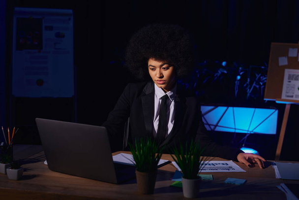 mujer de negocios afroamericana en ropa formal trabajando en la computadora portátil en la oficina oscura, turno de noche - Foto, Imagen