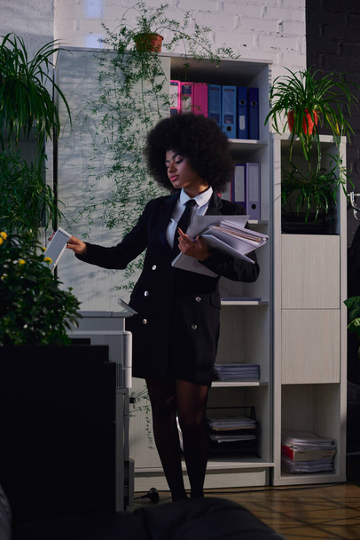 afro-américaine en élégant document de copie de vêtements formels tout en travaillant la nuit au bureau - Photo, image