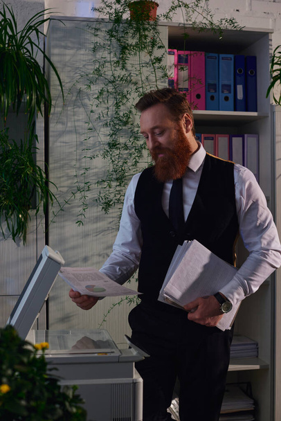 szakállas üzletember áll dokumentumok közelében fénymásoló gép, miközben dolgozik az irodában éjjel - Fotó, kép