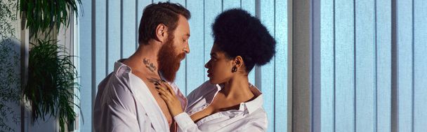 romance de oficina, hombre de negocios tatuado barbudo y mujer afroamericana abrazando por la noche, pancarta - Foto, imagen