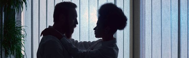 dark silhouette of african american woman embracing bearded businessman at night in office, banner - Photo, Image