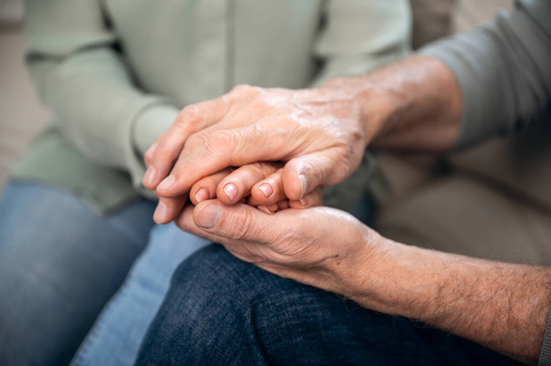 closeup of senior couple sitting on couch and holding hands, loving man supporting woman. understanding in marriage. elderly husband sincere gratitude his wife and sharing feelings - Photo, Image