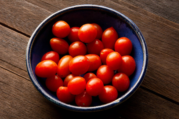 Un tazón de tomate cereza azul sobre una mesa de madera real en vista superior - Foto, imagen