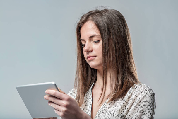 Nainen beige-sävyisessä paidassa lukee työtietoja tabletista. Hyödyntää internet, heijastaa teknologista kehitystä vuosisadan - Valokuva, kuva