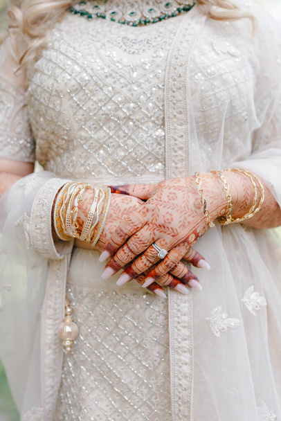 Руки индийской невесты украшены браслетами и узорами хны в индийском стиле. Руки невесты крупным планом с узорами и орнаментами в традиционном индийском стиле. Красивое платье невесты Индии - Фото, изображение