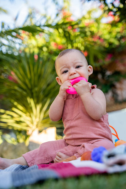 pequeño bebé sentado en el jardín en casa mordiendo un mordedor para aliviar el dolor de muelas. concepto primeros dientes, salud bucal y dentición del bebé - Foto, imagen