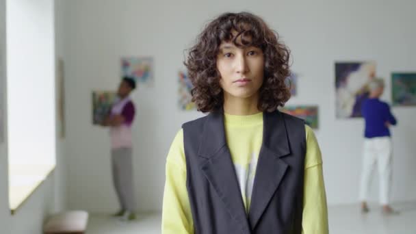 Retrato en la cintura de una mujer joven con el pelo rizado posando para la cámara en la galería de arte - Imágenes, Vídeo