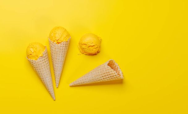 Лимонное мороженое в восхитительных вафельных рожках, лакомство для каждого вкусового рецептора. Над желтым фоном с копировальным пространством, плоский - Фото, изображение