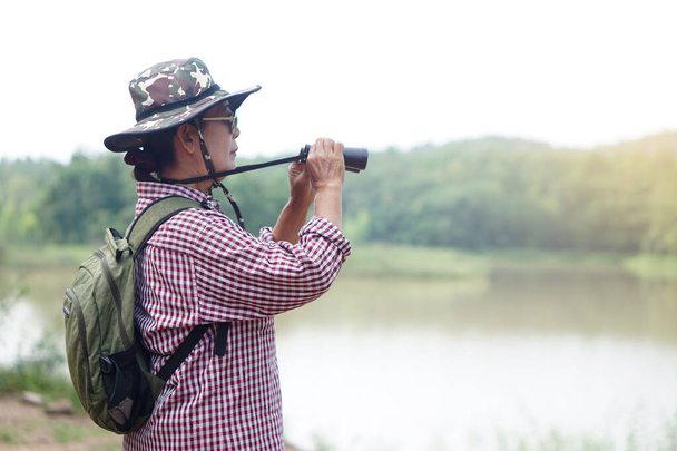 Mujer mayor asiática va a viajar sola, utilizar binocular para examinar la naturaleza en el lago. Concepto, actividad recreativa. Estilo de vida. Pase tiempo para viajar después de jubilarse.       - Foto, Imagen