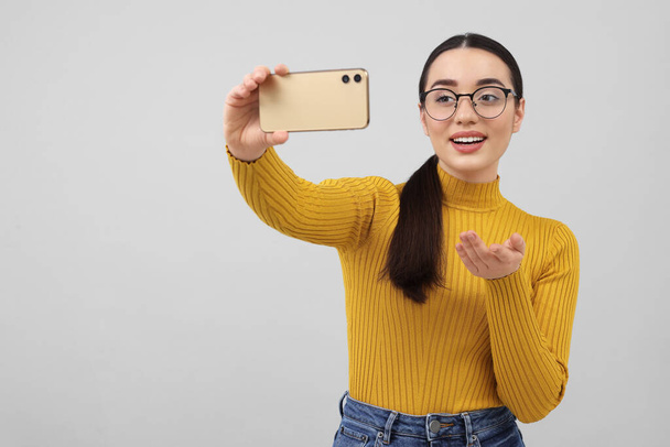 Smiling young woman taking selfie with smartphone on grey background, space for text - Fotoğraf, Görsel