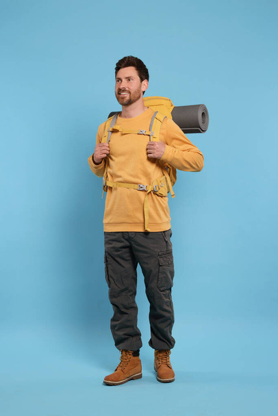 Happy man with backpack on light blue background. Active tourism - Foto, afbeelding