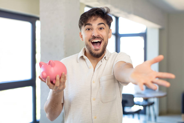 young handsome man smiling happily and offering or showing a concept. piggy bank concept - 写真・画像