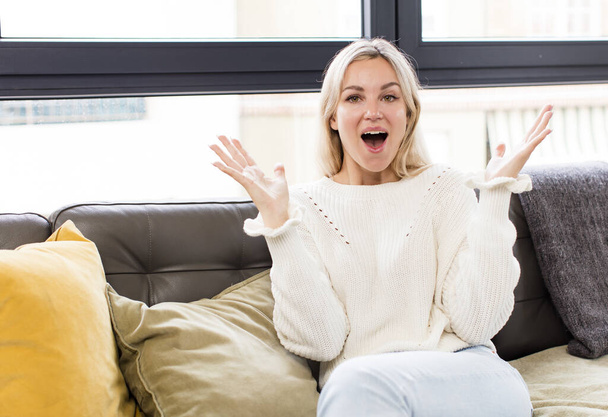 young pretty woman feeling happy, excited, surprised or shocked, smiling and astonished at something unbelievable sitting on a couch - Фото, зображення