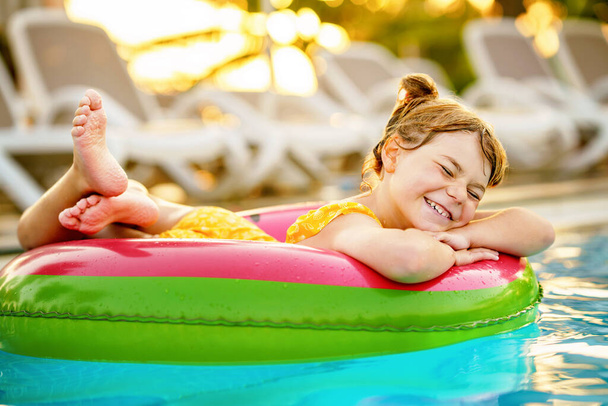 Šťastná holčička s nafukovacím kroužkem plave v bazénu. Malé předškolní dítě se učí plavat a potápět ve venkovním bazénu hotelového resortu. Zdravá sportovní aktivita a zábava pro děti - Fotografie, Obrázek