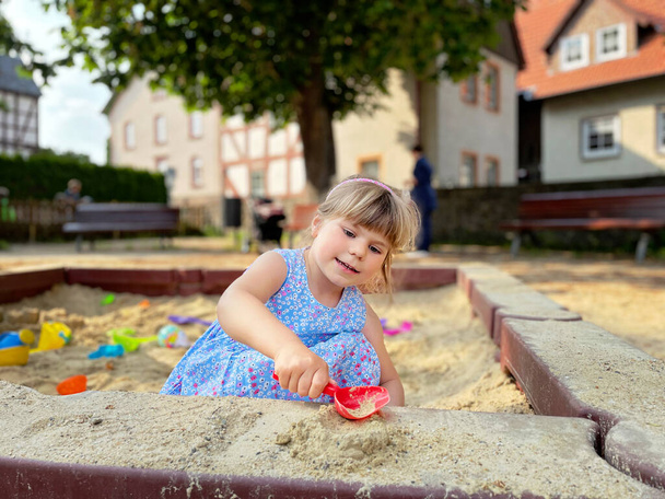 Adorable niña en el patio de recreo en la arena. Niño jugando con moldes de arena y haciendo mudpies. Actividades creativas al aire libre para niños - Foto, Imagen
