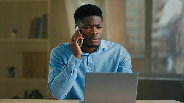 Afrikai férfi üzletember etnikai 30-as évek férfi irodai dolgozó munka távol otthoni beszélgetés üzleti beszélgetés mobiltelefon vezeték nélküli hívás megvitatása projekt nézd laptop képernyő használata mobiltelefon okostelefon - Fotó, kép