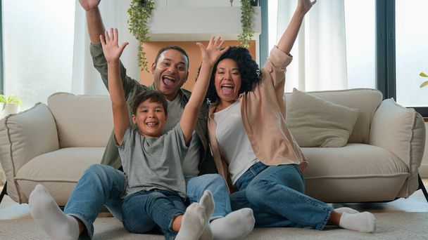 Happy multiracial family African American parents Caucasian child little boy on floor in living room own apartment mom dad kid home celebration excited father mother son raise hands together fun joy - Photo, Image