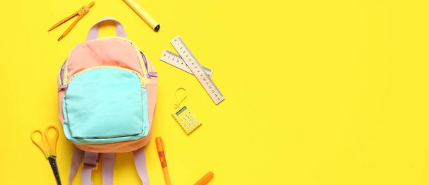 Школьный рюкзак и различные канцелярские принадлежности на желтом фоне с местом для текста - Фото, изображение