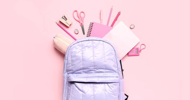 Mochila escolar y diferentes artículos de papelería sobre fondo rosa, vista superior - Foto, Imagen