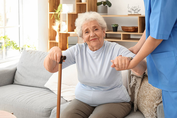 Pflegerin hilft Seniorin, zu Hause aufzustehen - Foto, Bild
