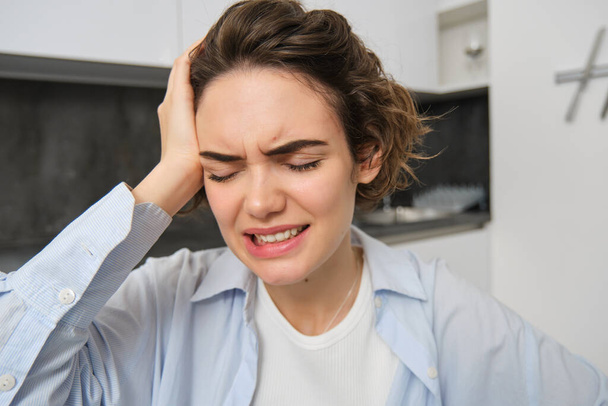 Porträt einer brünetten Frau berührt ihren Kopf, Grimassen vor Schmerzen, hat Kopfschmerzen, schmerzhafte Migräne. - Foto, Bild