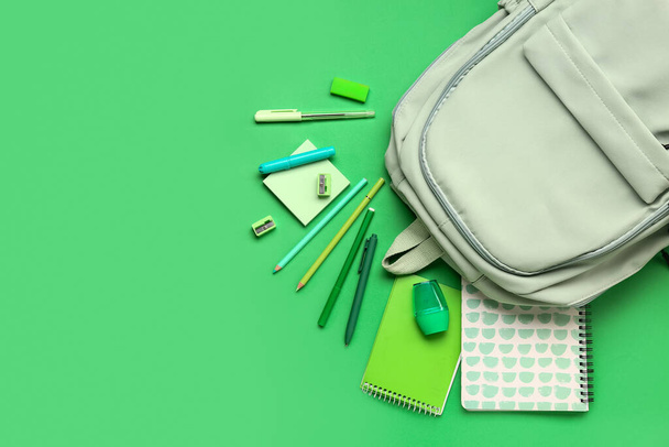 Stilvoller Schulrucksack mit verschiedenen Schreibwaren auf grünem Hintergrund - Foto, Bild