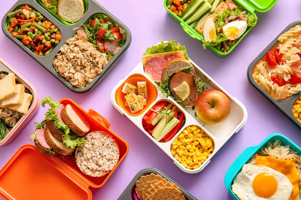 Veel lunchboxen met verschillende heerlijke gerechten op lila achtergrond - Foto, afbeelding