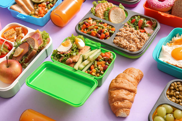 Viele Lunchboxen mit verschiedenen leckeren Speisen auf fliederfarbenem Hintergrund - Foto, Bild