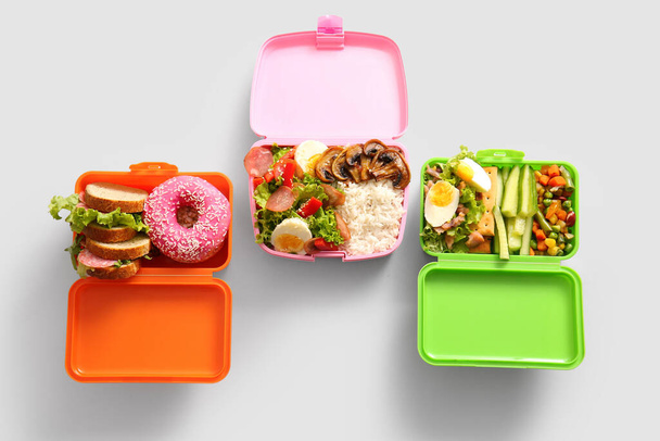 Cajas de almuerzo con diferentes alimentos deliciosos sobre fondo gris - Foto, Imagen