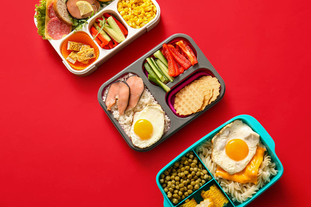 Lunchboxen met verschillende heerlijke gerechten op rode achtergrond - Foto, afbeelding