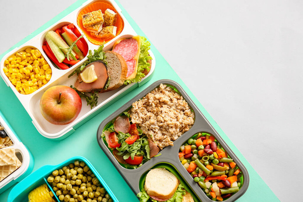 Cajas de almuerzo con diferentes alimentos deliciosos en el fondo de color - Foto, Imagen