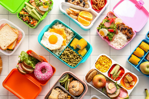 Viele Lunchboxen mit verschiedenen leckeren Speisen auf weißem Fliesenhintergrund - Foto, Bild