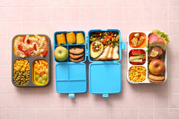 Обеденные коробки с различными вкусными блюдами на розовом фоне плитки - Фото, изображение