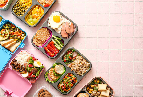 Lunchboxes με διαφορετικά νόστιμα τρόφιμα σε ροζ φόντο πλακιδίων - Φωτογραφία, εικόνα