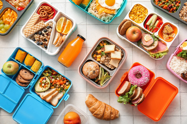 Viele Lunchboxen mit verschiedenen leckeren Speisen und einer Flasche Saft auf weißem Fliesenhintergrund - Foto, Bild
