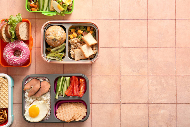 Scatole da pranzo con diversi cibi deliziosi su sfondo di piastrelle rosa - Foto, immagini