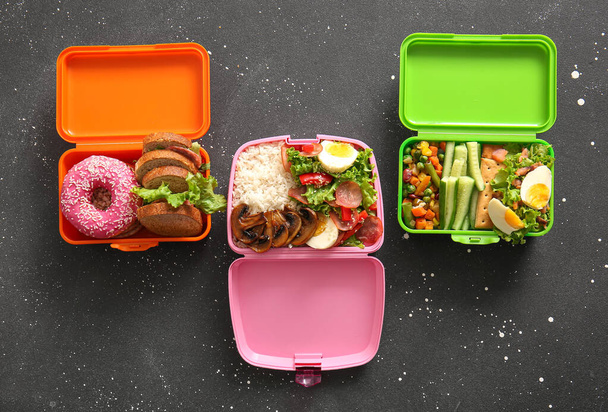 Veel lunchboxen met verschillende heerlijke gerechten op grunge zwarte achtergrond - Foto, afbeelding