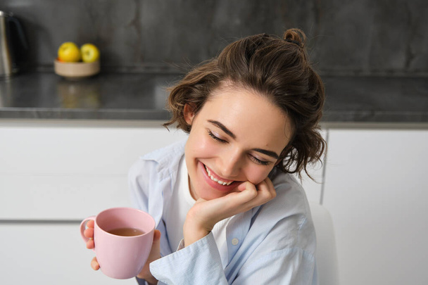 Bom dia. Retrato de mulher morena feliz, bebe xícara de café em sua cozinha e sorrindo, início acolhedor e quente do dia com cuppa. - Foto, Imagem